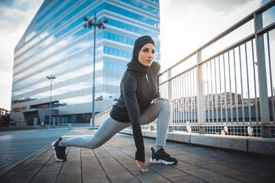 Beautiful woman wearing hijab exercising against building during sunrise