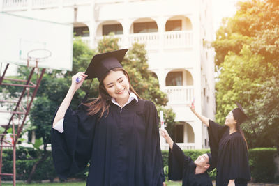 Cheerful student in graduation gown standing outdoors