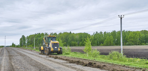 Road grader working on rural dirt road beside farmland