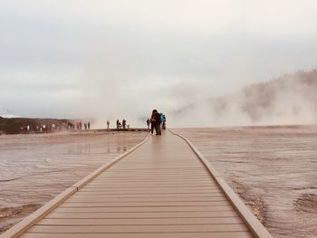 People on boardwalk at hot spring against sky