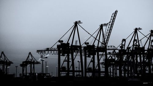 Silhouette cranes at construction site against clear sky