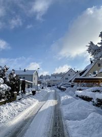 Snow covered road amidst buildings against sky