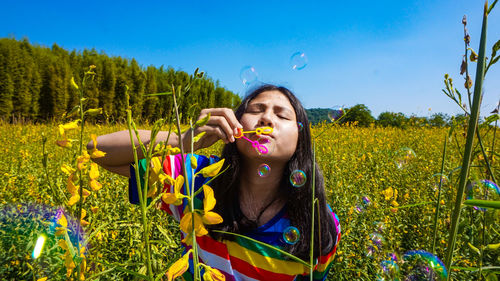 Girl blowing bubbles on field during sunny day