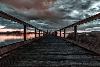 Footbridge over suspension bridge against cloudy sky