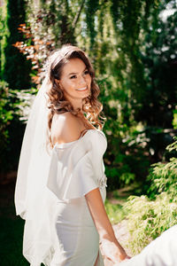 Portrait of smiling young woman standing against trees