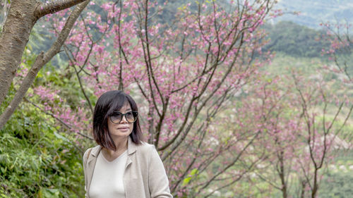 Young woman standing against cherry blossom tree