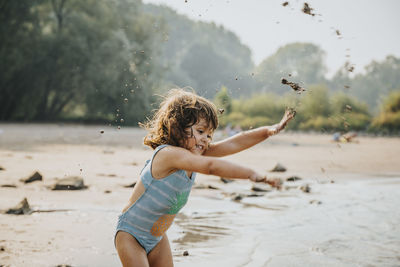 Cute girl throwing sand and mud while standing at beach