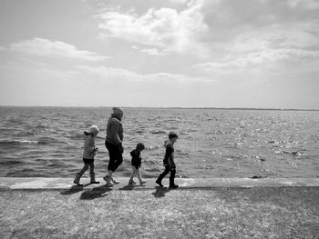 Rear view of woman walking at beach against sky