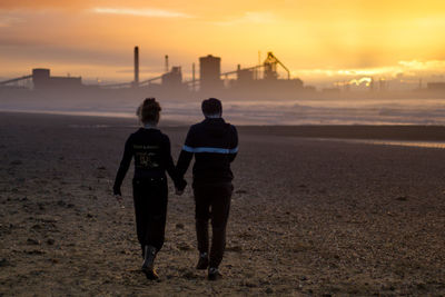 Rear view of friends on beach against sky during sunset