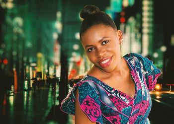 Portrait of smiling young woman on illuminated city street at night