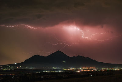 Lightning over illuminated cityscape against sky at night