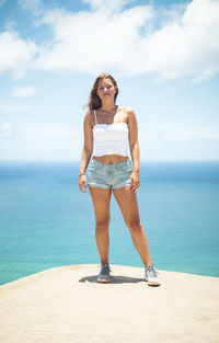 Full length of young woman standing in sea against sky