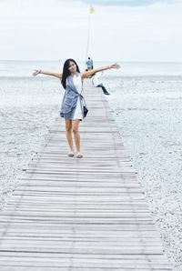 Full length of woman standing on pier by sea against sky