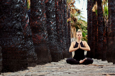 Full length of woman meditating while sitting at public park