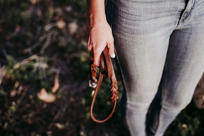 Midsection of woman holding leather belt while standing on land