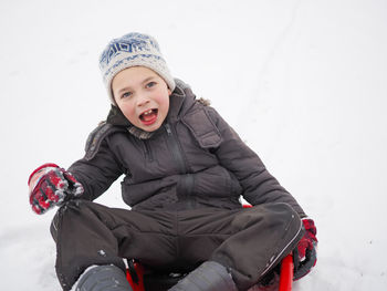 Portrait of playful boy tobogganing on snow during winter