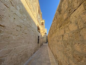 Low angle view of alley amidst wall against sky