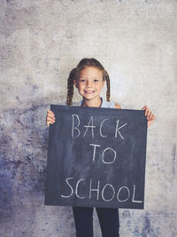 Portrait of smiling girl holding writing slate with text against wall