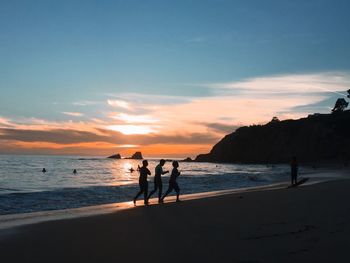 Silhouette friends walking at beach against sky during sunset