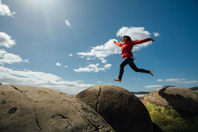 Low angle view of woman jumping on rocks against sky during summer