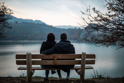 Rear view of man sitting on bench against sky