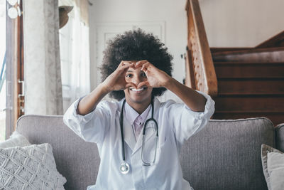 Portrait of doctor making heart shape sitting at home