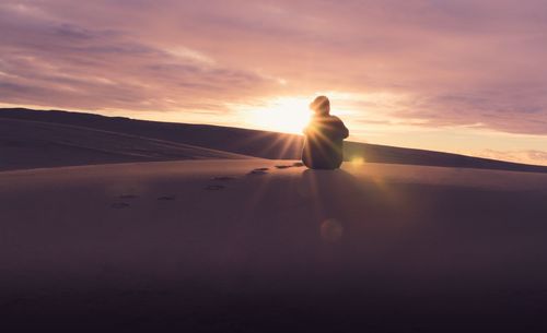 Man on sand dune against sky during sunset