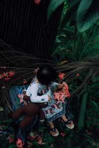 High angle view of girl sitting with teddy bear on leaves amidst plants