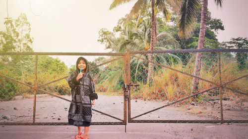 Smiling boy standing on road against closed gate