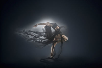 Young woman dancing on box against black background