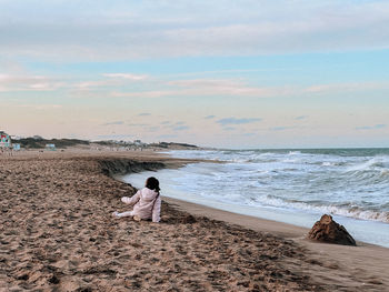 Rear view of woman standing at beach against sky