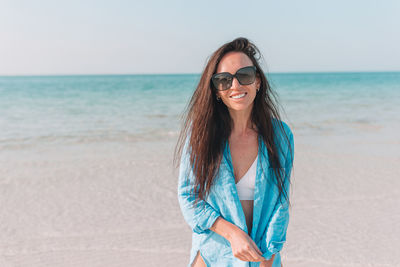 Portrait of young woman wearing sunglasses standing on beach