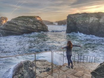 Rear view of woman standing on rock by sea against sky