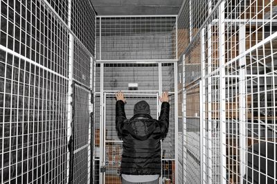 Rear view of a man standing against fence in room