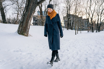 A woman in a coat, scarf, hat and boots walks in the snow in winter