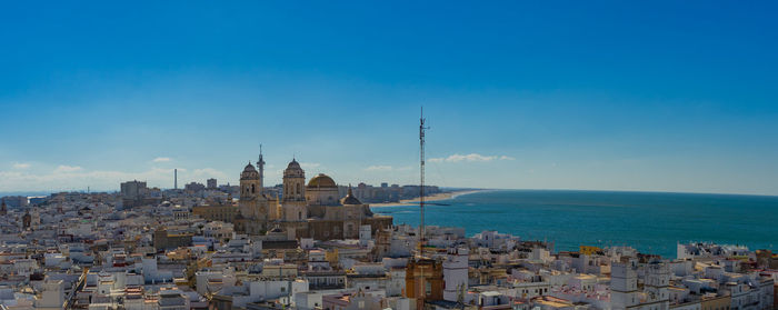 Cityscape by sea against blue sky