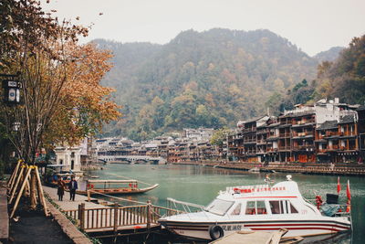 Boats moored on river by trees against mountains