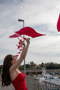 Side view of woman holding red bunting against sky