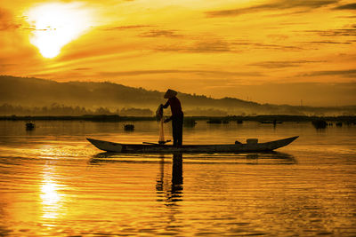 Silhouette fisherman fishing at lake against orange sky