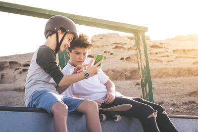 Two young boy using smartphone at the skate park, sitting on an halfpipe ramp. teenagers communicate