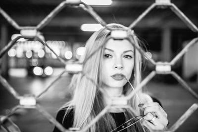 Portrait of young woman standing at parking garage seen through fence