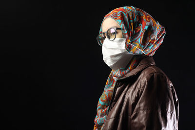 Side view of woman wearing surgical mask against black background