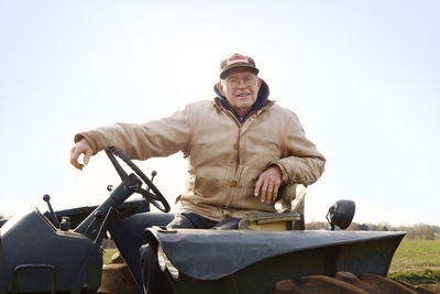 Portrait of confident farmer driving tractor against sky
