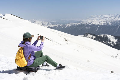 Rear view of man sitting on snowcapped mountain