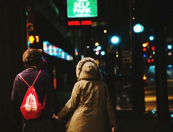 Rear view of man and woman on illuminated city street at night