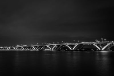 Illuminated bridge over river against sky at night