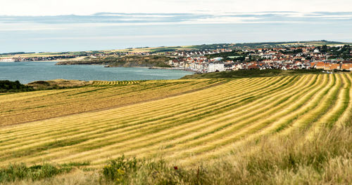 Scenic view of field by town against sky and sea