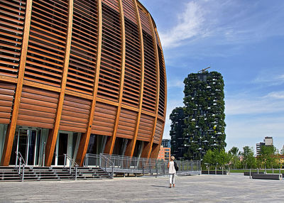 Woman standing by modern building in city against sky