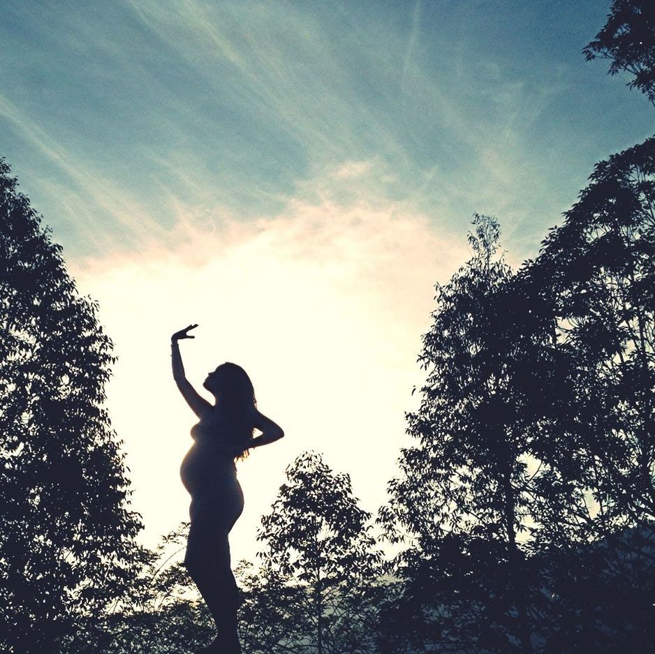 low angle view, tree, sky, silhouette, human representation, statue, sculpture, mid-air, art and craft, art, creativity, cloud - sky, nature, outdoors, day, cloud, bird, tranquility, one person