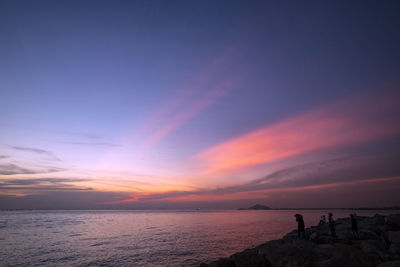 Silhouette people on beach against sky during sunset